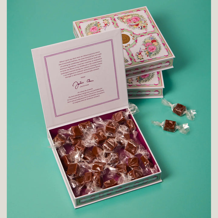 Open box of wrapped candies with a decorative lid on a teal background