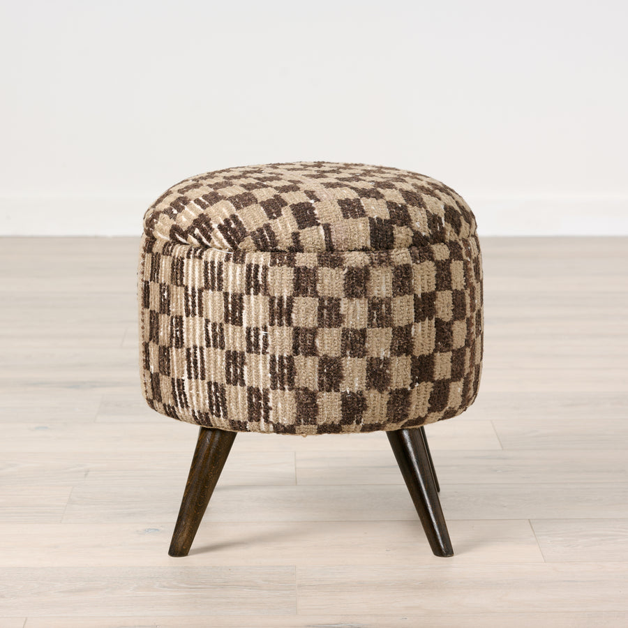 Checkered patterned ottoman with wooden legs on a light wood floor.