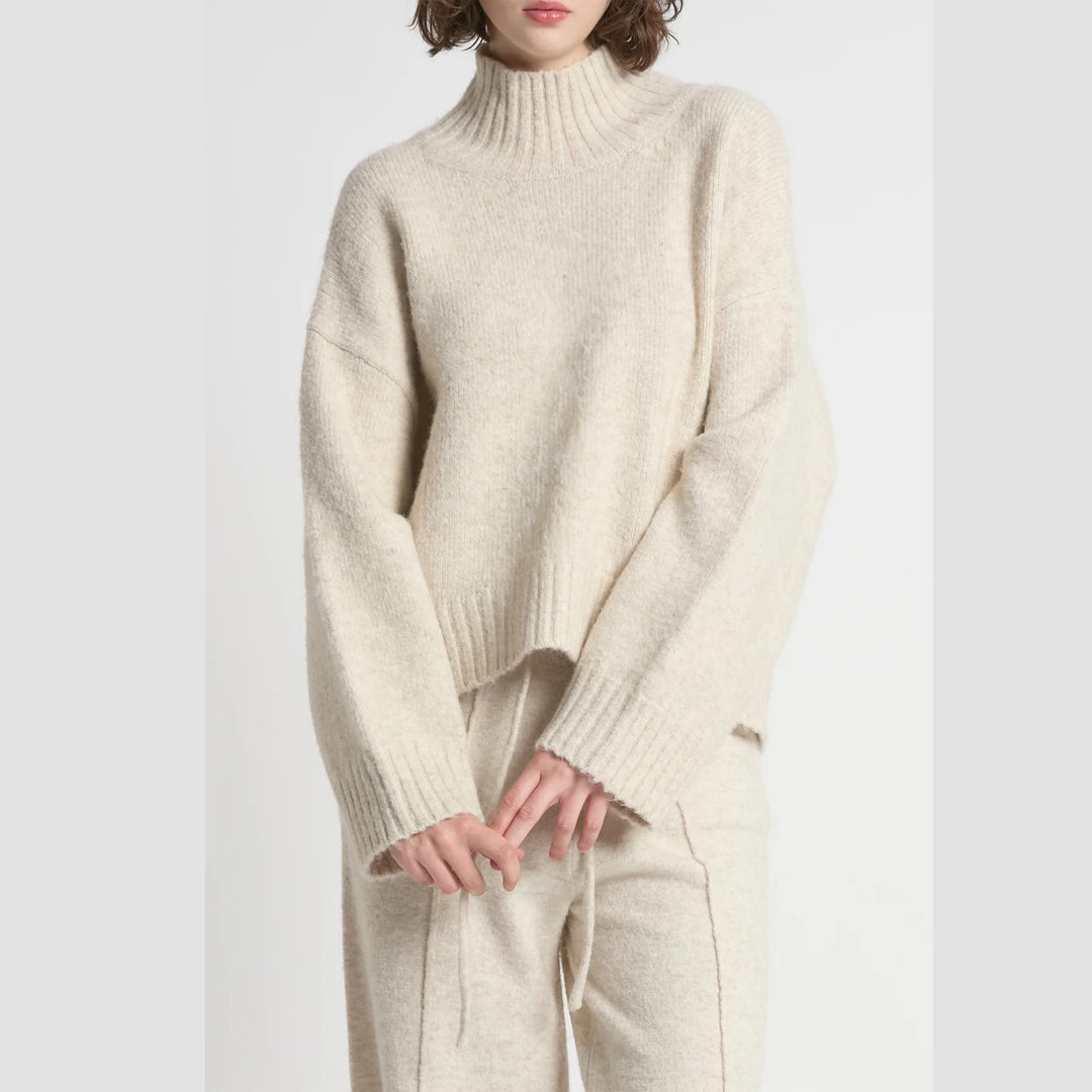 Person wearing a cream-colored sweater and pants on a white background