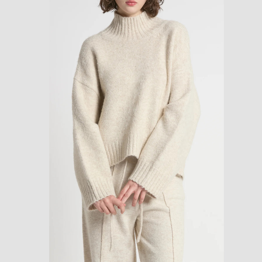 Person wearing a cream-colored sweater and pants on a white background