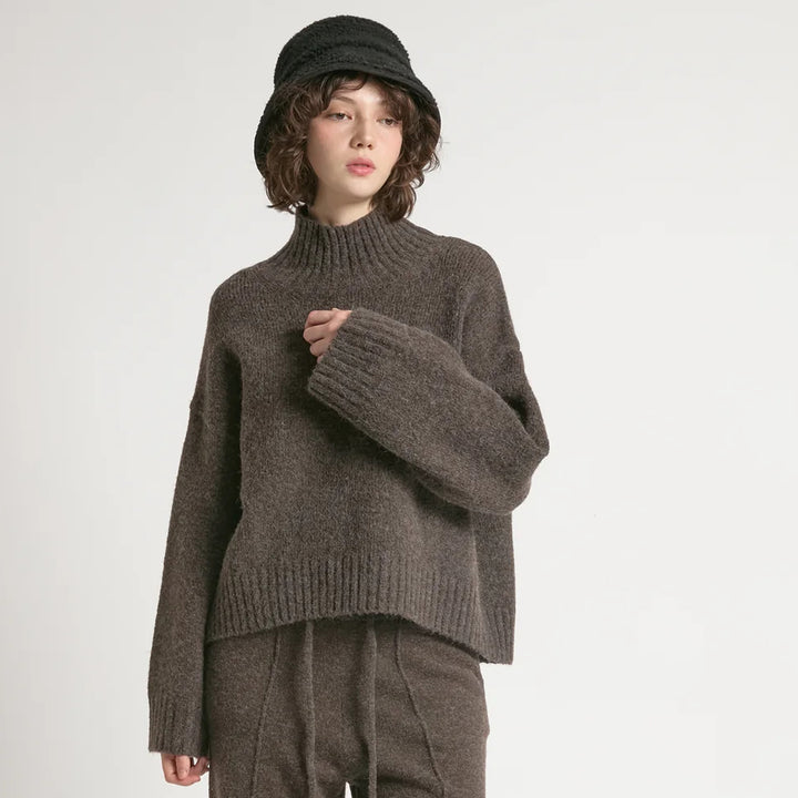 Person wearing a brown knitted sweater and matching pants on a white background