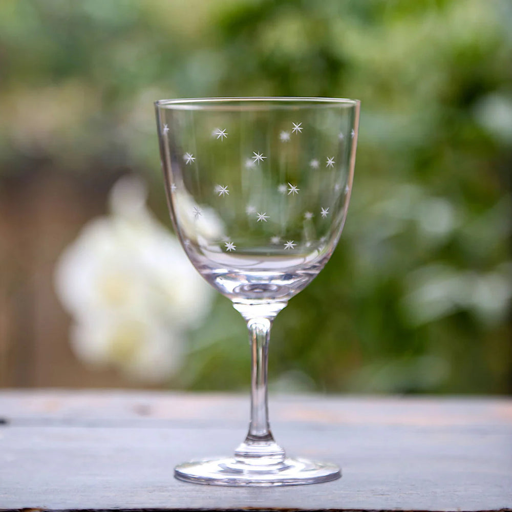 Clear glass wine glass with star patterns on a wooden surface with a blurred green background