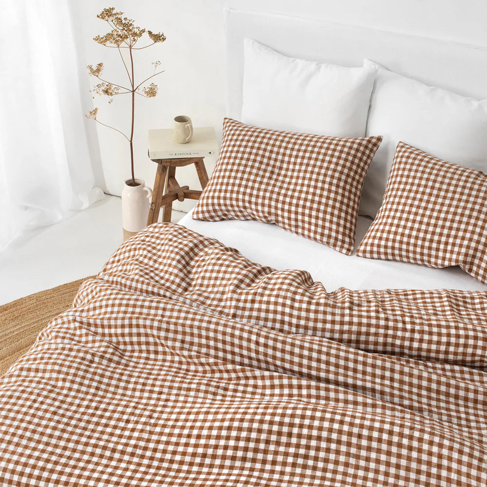 Brown and white checkered bedding set on a bed with a white wall and plant in the background.