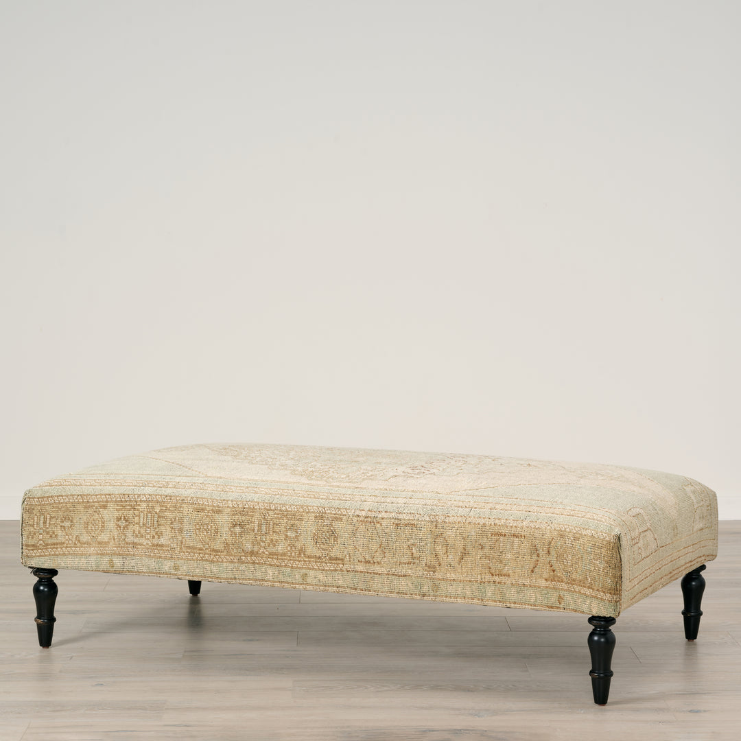 Beige upholstered bench with black legs on a neutral background