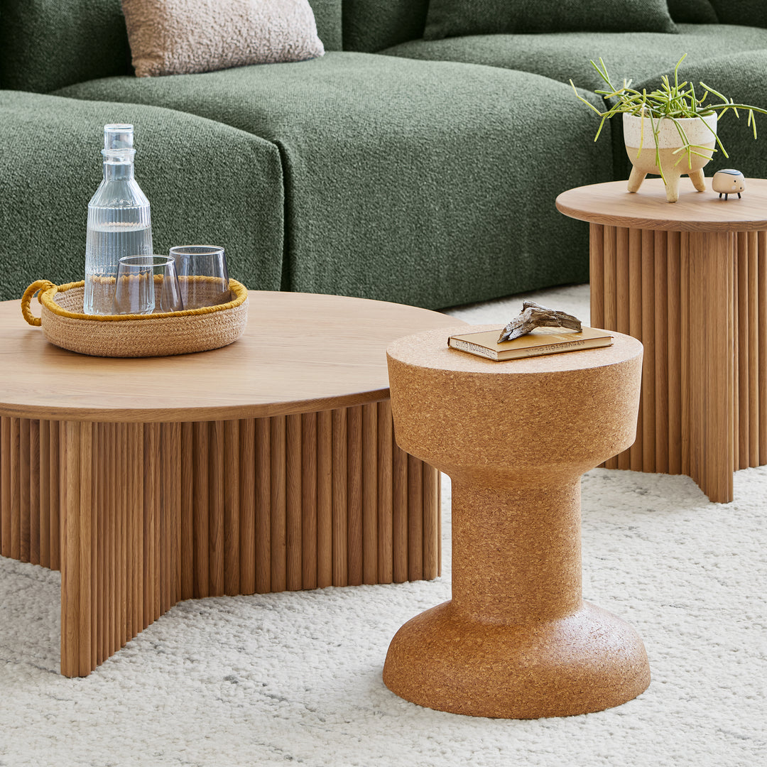 Wooden coffee table with a bottle and glasses, surrounded by green sofas and decorative items.