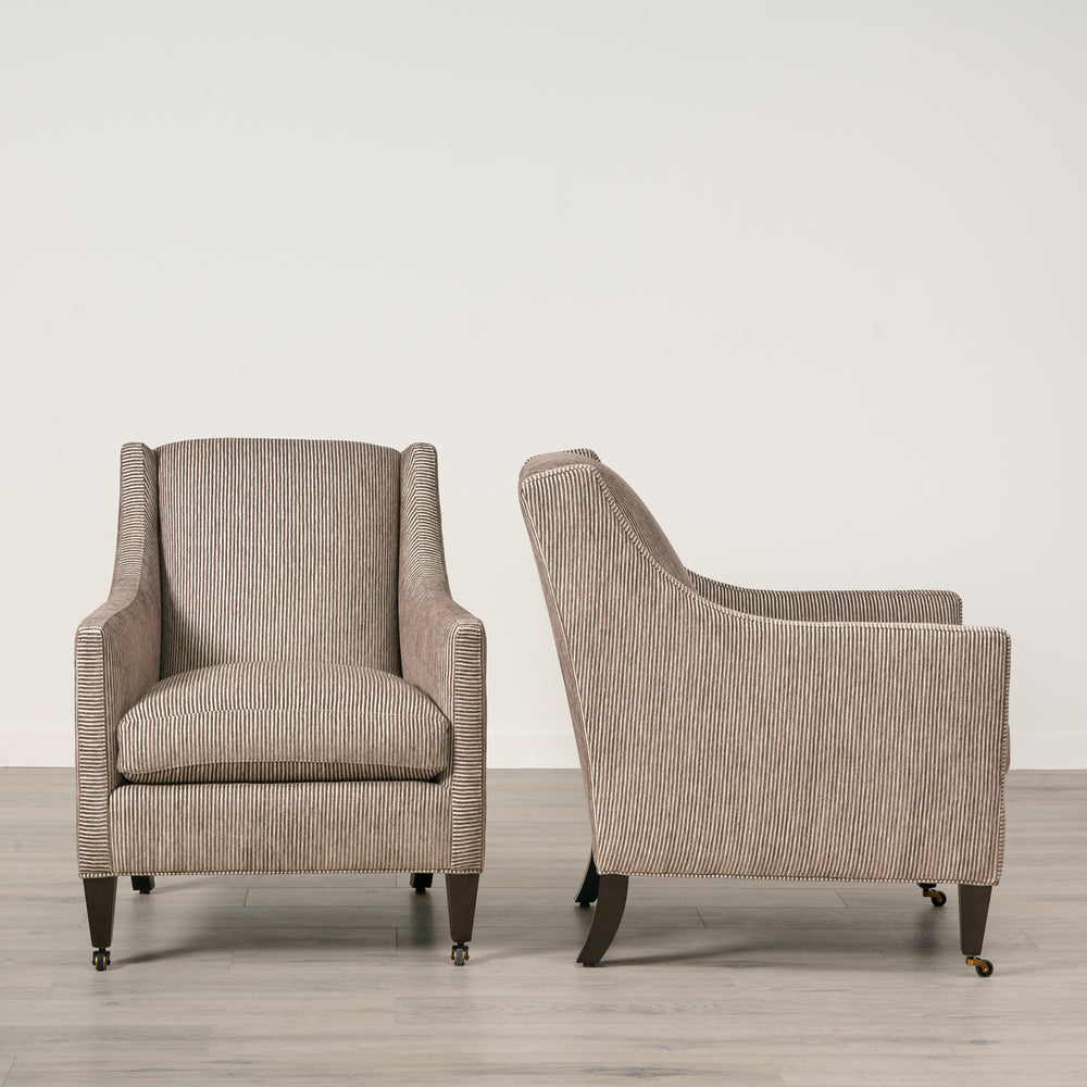 Two beige armchairs on a wooden floor with a light gray wall background