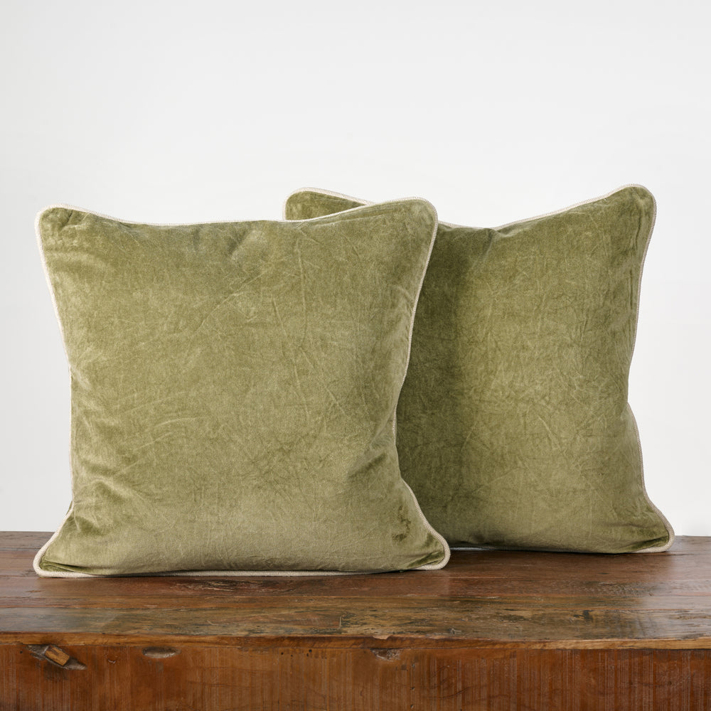 Two green velvet pillows on a wooden surface with a white background