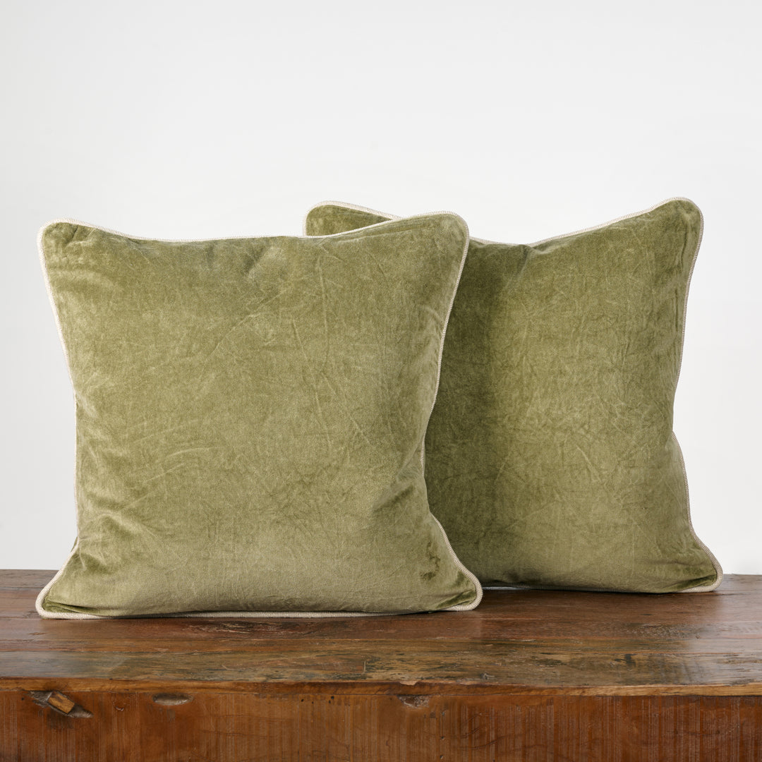 Two green velvet pillows on a wooden surface with a white background