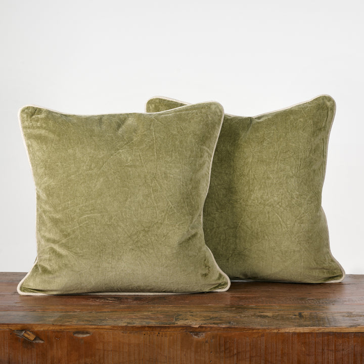 Two green velvet pillows on a wooden surface with a white background