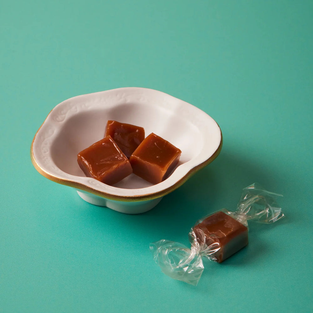 Caramel candies in a white bowl on a teal background