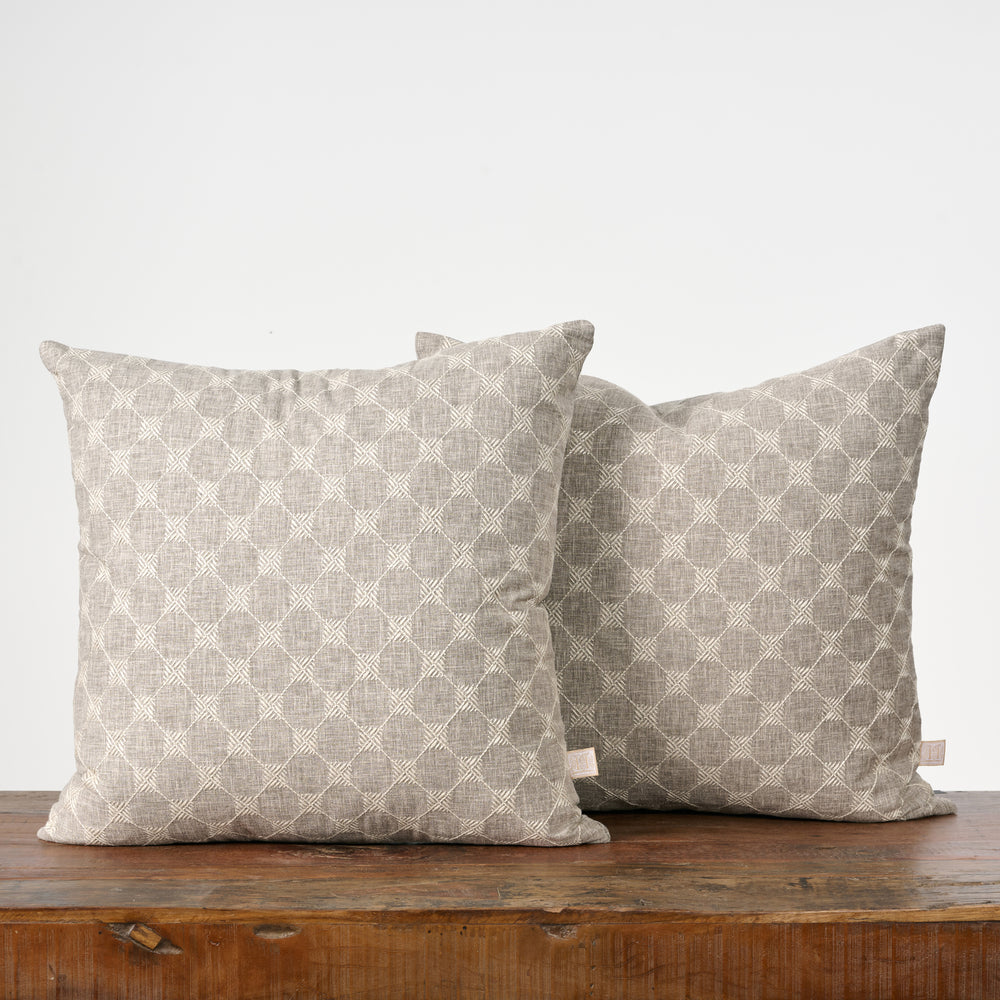Two patterned pillows on a wooden surface with a white background
