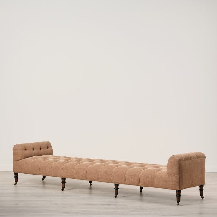 Beige upholstered bench on a wooden floor with a plain white wall background