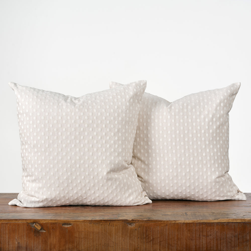 Two white pillows with a subtle pattern on a wooden surface against a light background