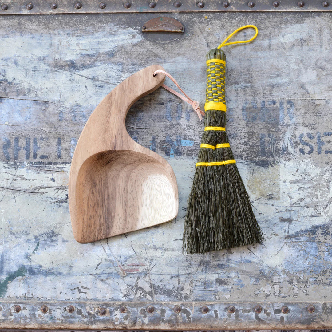 Wooden dustpan and broom with straw handle on a textured metal surface