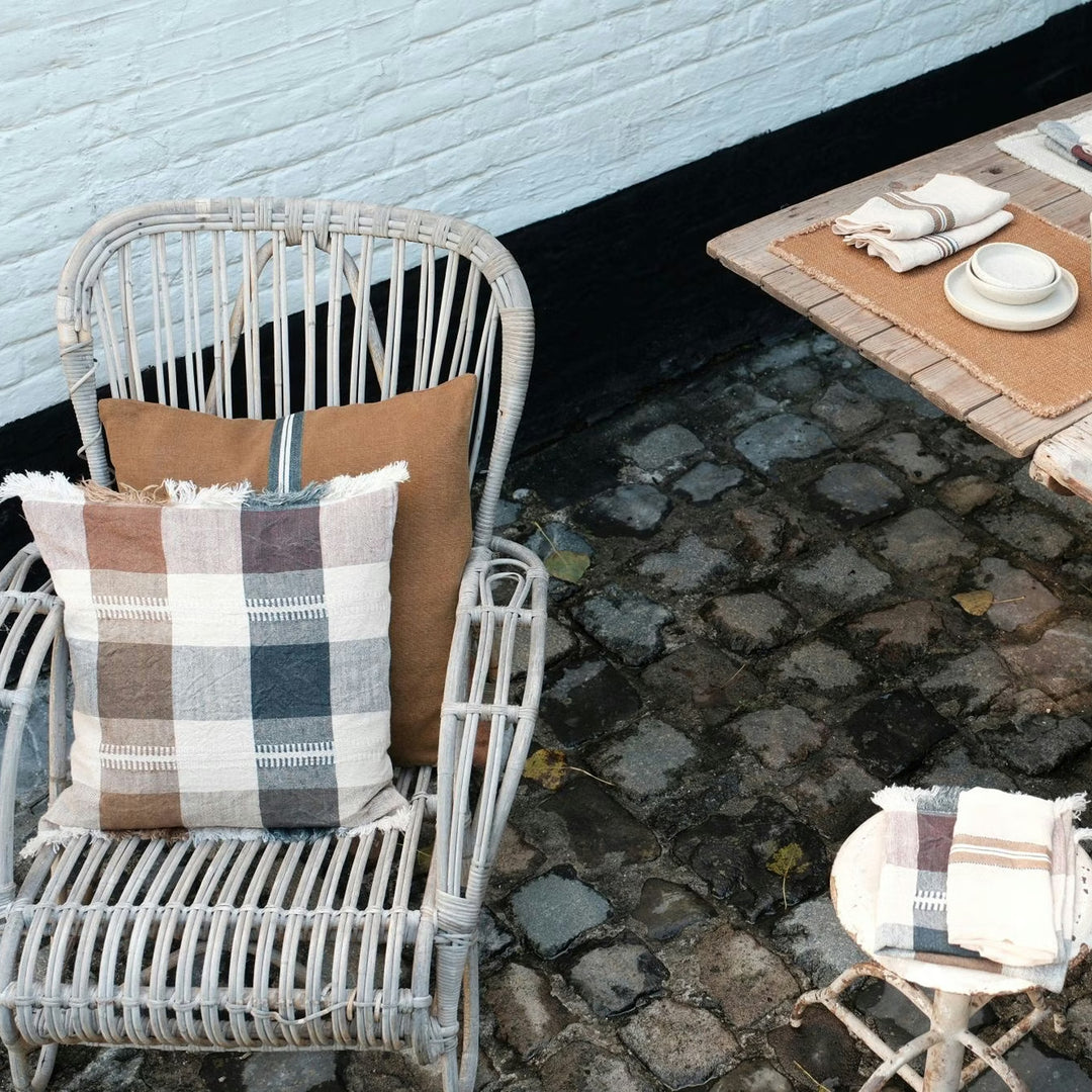 Wicker chair with plaid cushions on a stone patio next to a table with a placemat.
