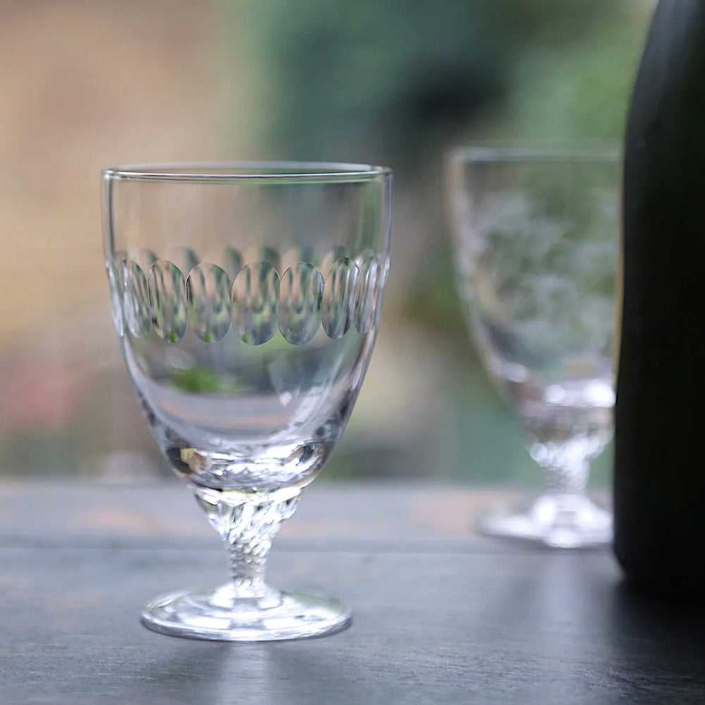 Clear glass goblet with decorative rim on a blurred natural background