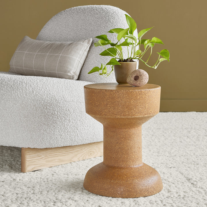 Brown side table with a plant on it next to a white sofa with gray cushions.