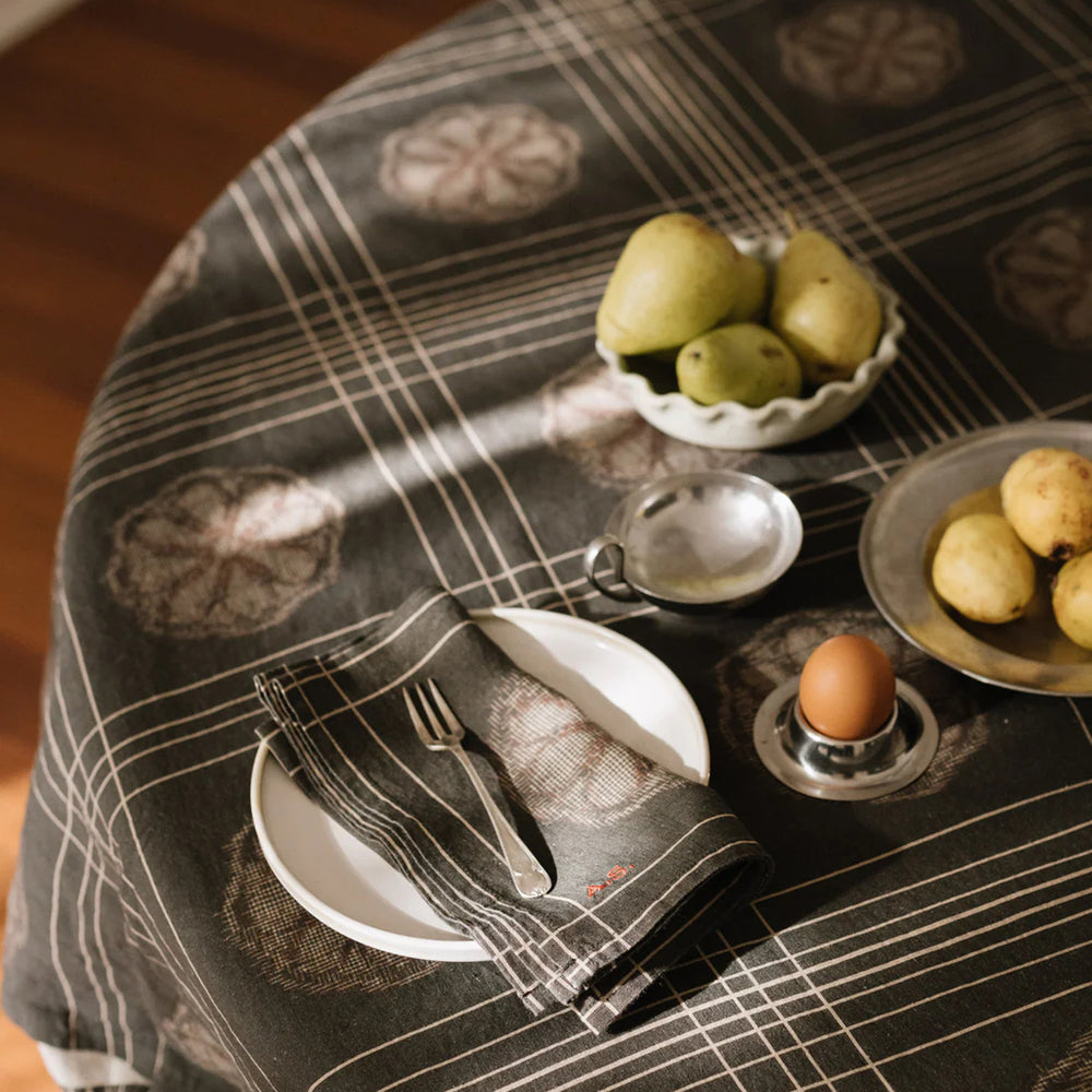 Table setting with plates, napkin, and fruit on a patterned tablecloth.