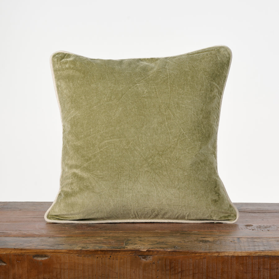 Green velvet pillow on a wooden surface with a white background