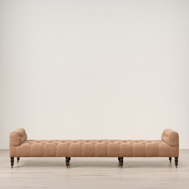 Beige tufted bench on a light wooden floor with a white wall background