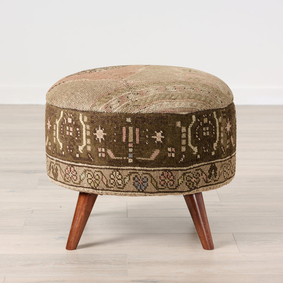 Round ottoman with patterned cushion and wooden legs on a light wood floor.