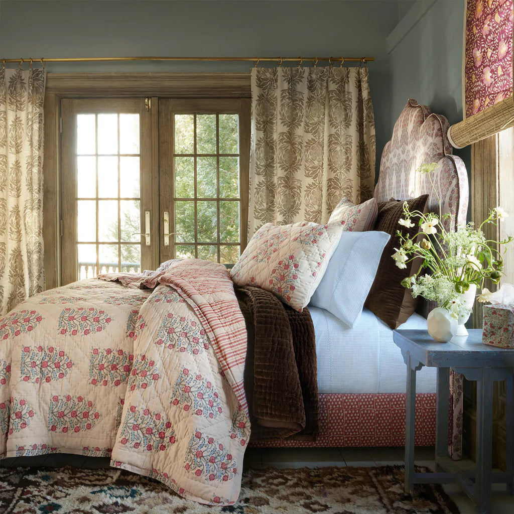 Bedroom with floral bedding, curtains, and a side table with flowers.