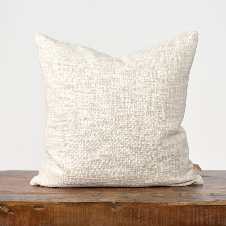 Beige textured pillow on a wooden surface with a light gray background