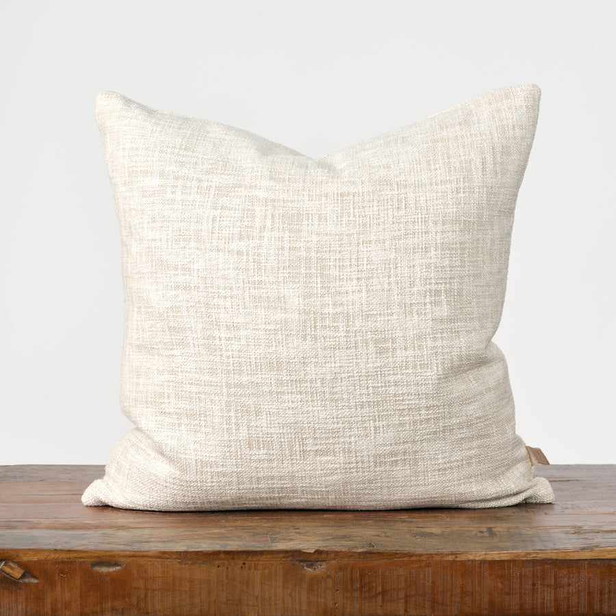 Beige textured pillow on a wooden surface with a light gray background