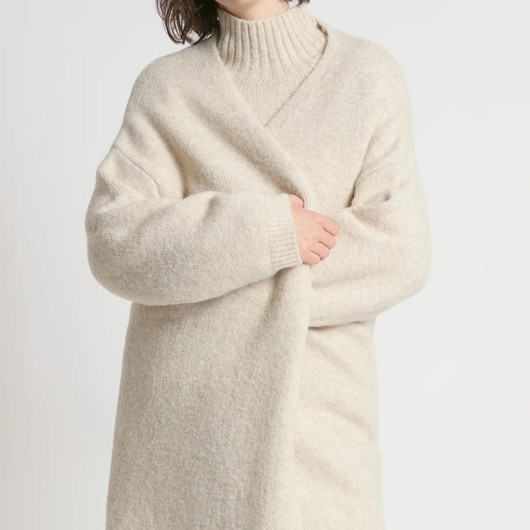 Person wearing a long beige sweater against a light gray background