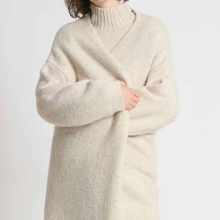 Person wearing a long beige sweater against a light gray background