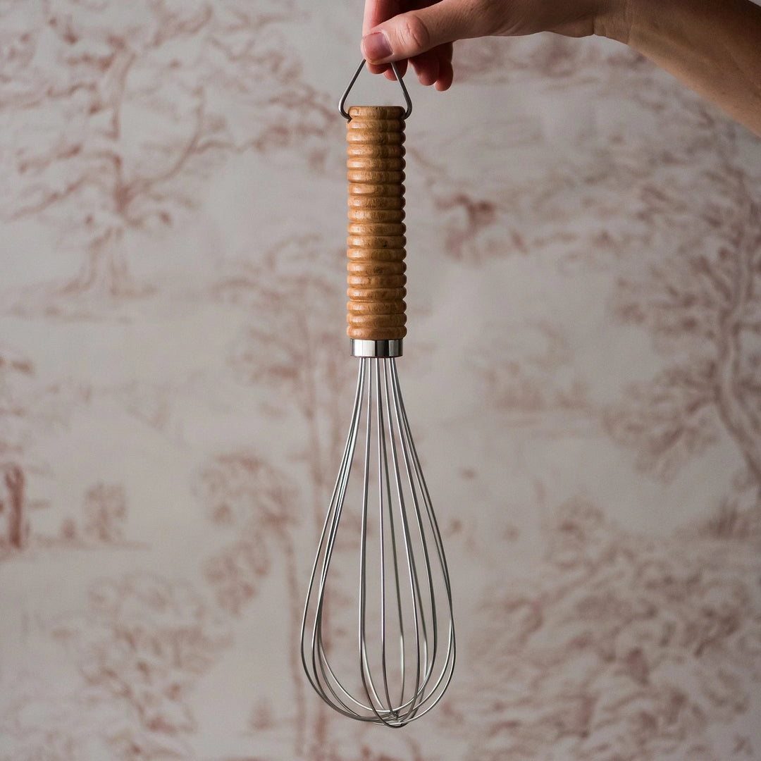 Hand holding a whisk with a wooden handle against a marble background