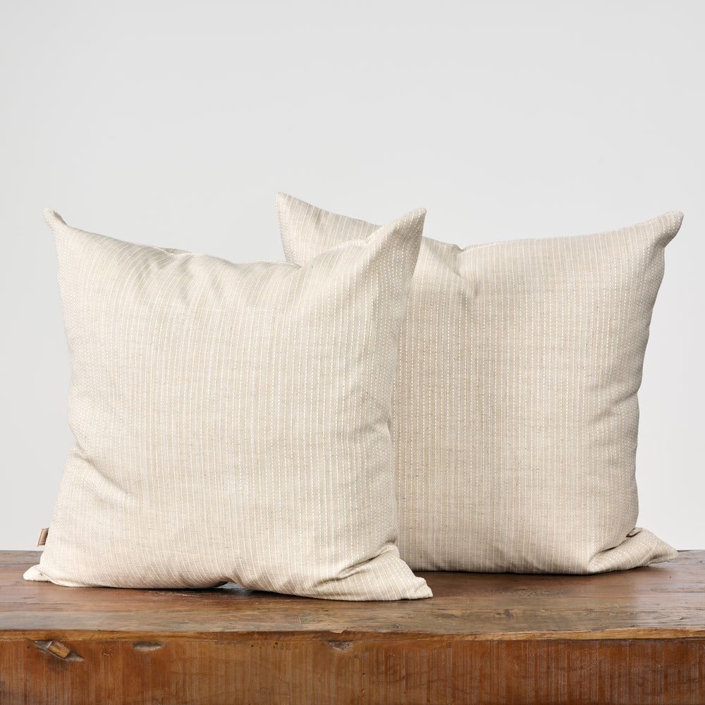 Two beige pillows on a wooden surface with a light gray background