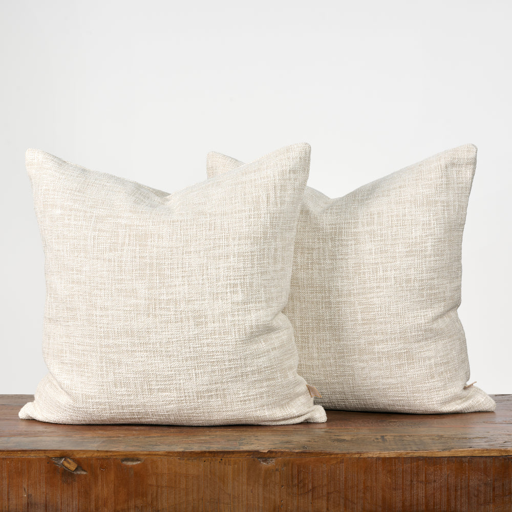 Two beige textured pillows on a wooden surface with a white background