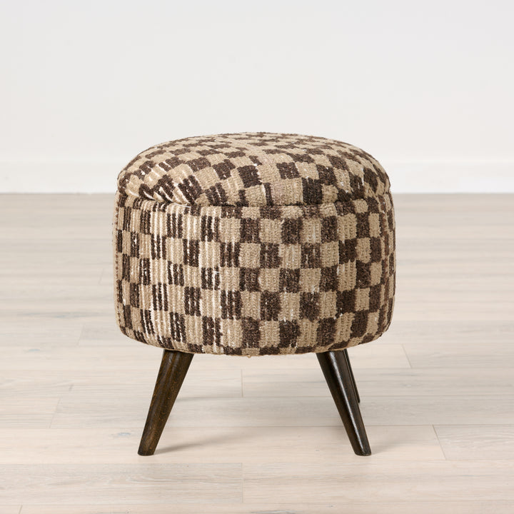 Checkered patterned ottoman with wooden legs on a light wood floor.