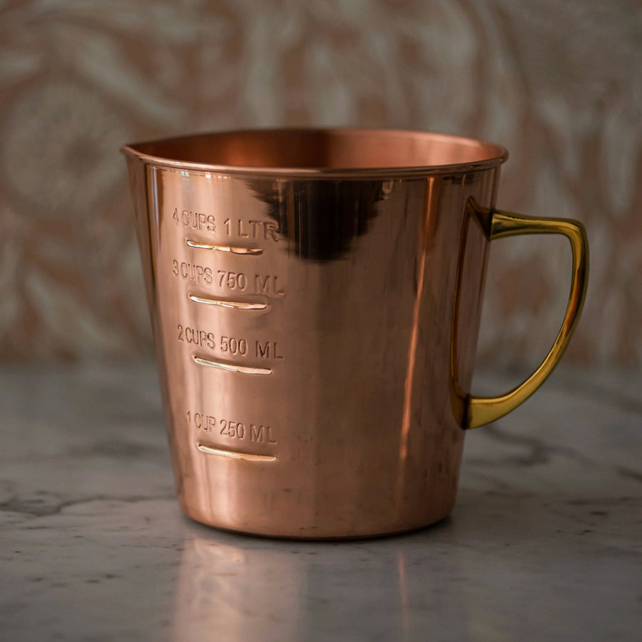 Copper measuring cup with gold handle on a reflective surface