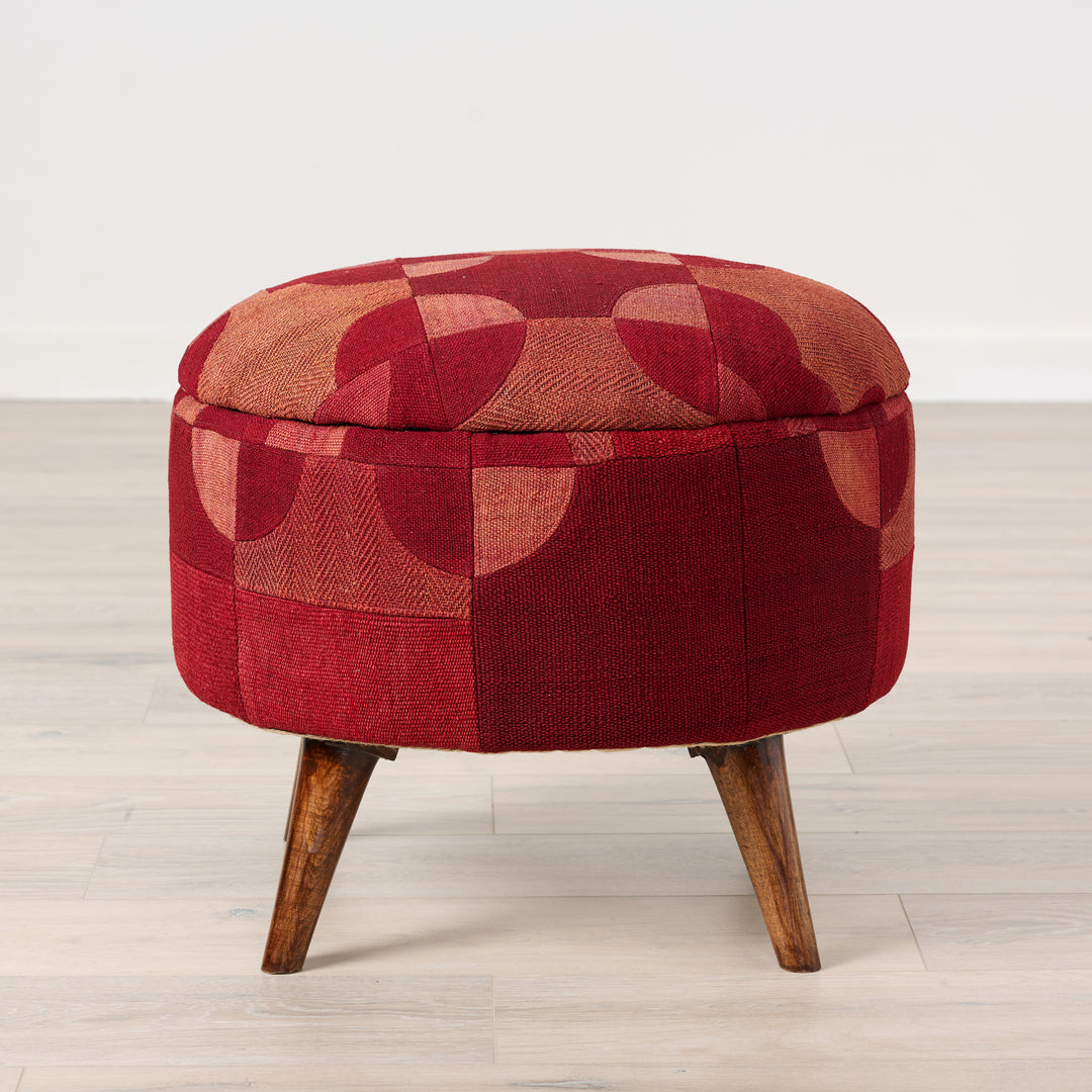 Red patterned ottoman with wooden legs on a light wood floor.