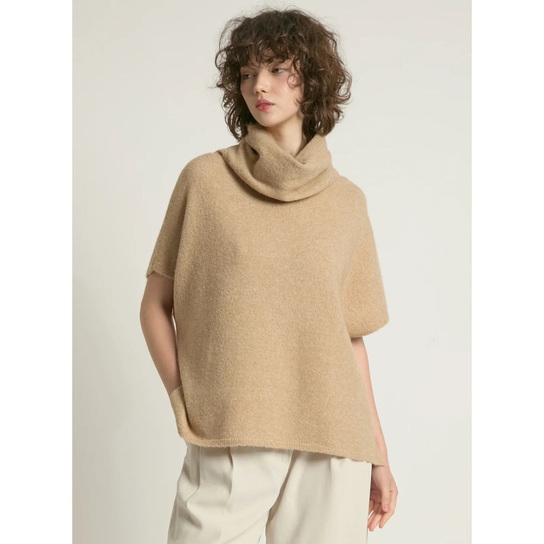 Woman wearing a beige poncho against a plain background