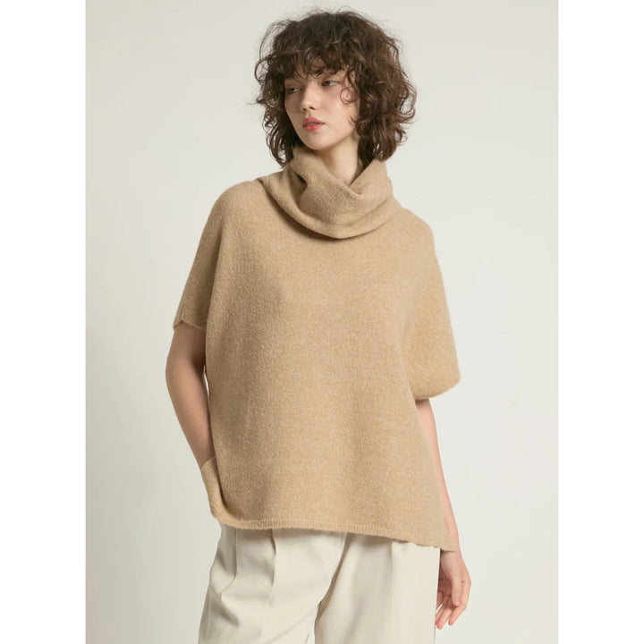 Woman wearing a beige poncho against a plain background