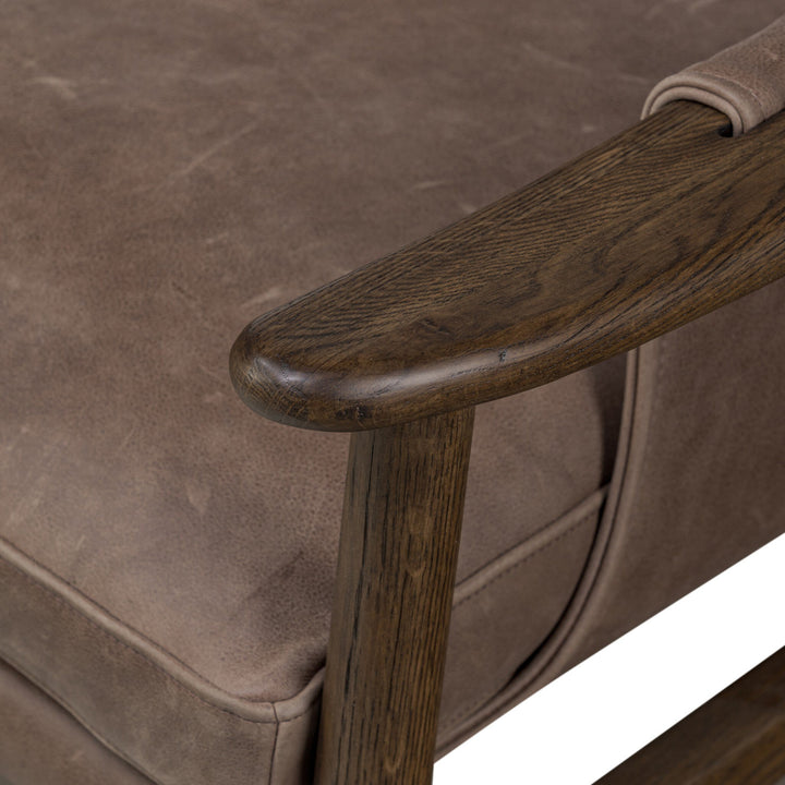 Close-up of a brown leather armchair with wooden armrest.