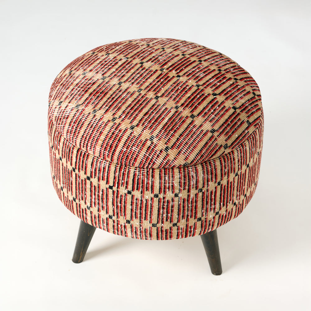 Round ottoman with patterned fabric and wooden legs on a white background