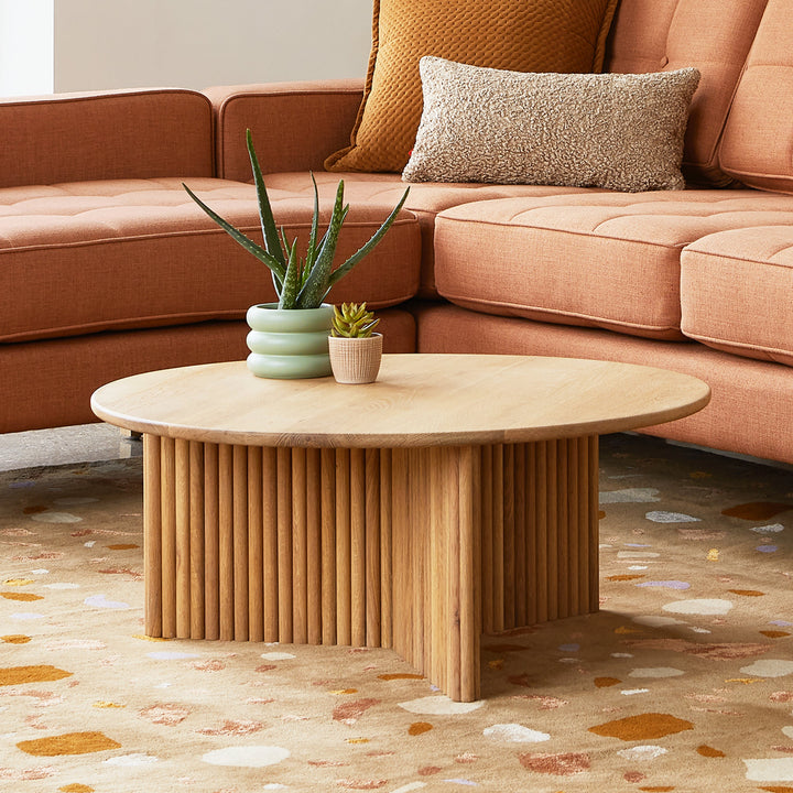 Wooden coffee table with two small plants in front of a beige sofa.