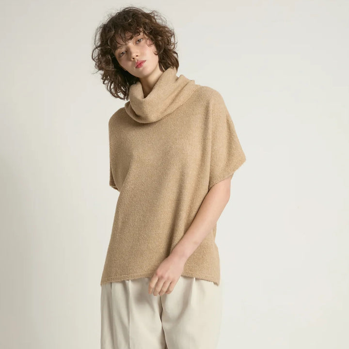 Person wearing a beige cowl-neck sweater against a plain background