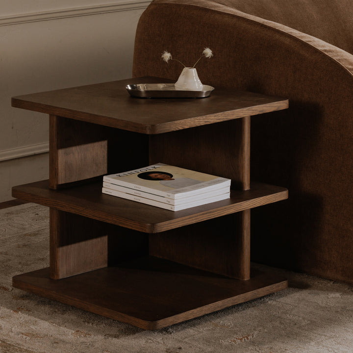 Wooden side table with books and a tray against a brown wall.